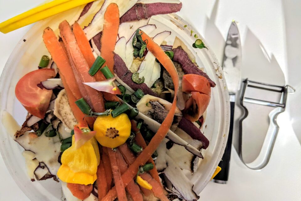 Compostor de lemn într-o grădină, cu resturi vegetale și frunze uscate în straturi