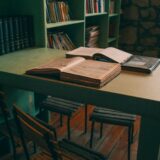 Cărți deschise pe o masă de lemn într-o bibliotecă liniștită, luminată natural