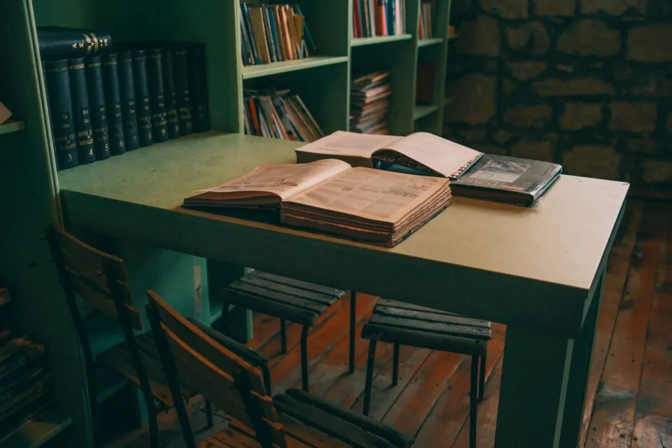 Cărți deschise pe o masă de lemn într-o bibliotecă liniștită, luminată natural