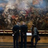 Vizitator așezat pe o bancă, privind atent un tablou mare într-o sală de muzeu