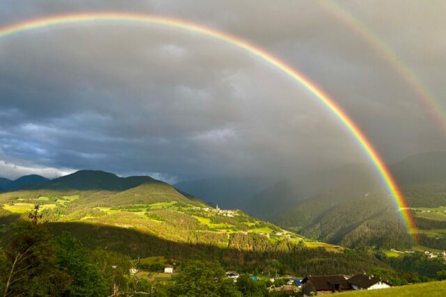 Curcubeu dublu deasupra unui câmp verde, după o ploaie de vară